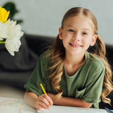 girl with pigtails drawing and smiling at the camera